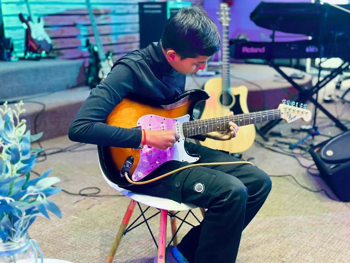 A young boy sitting on a white chair playing an electric guitar in a music studio
