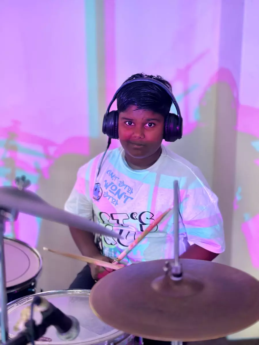 Young boy wearing headphones playing drums with colourful projection lighting