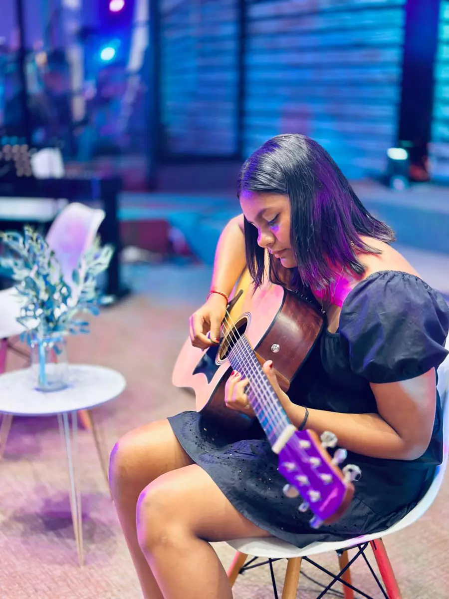 Young woman playing acoustic guitar with blue-lit background