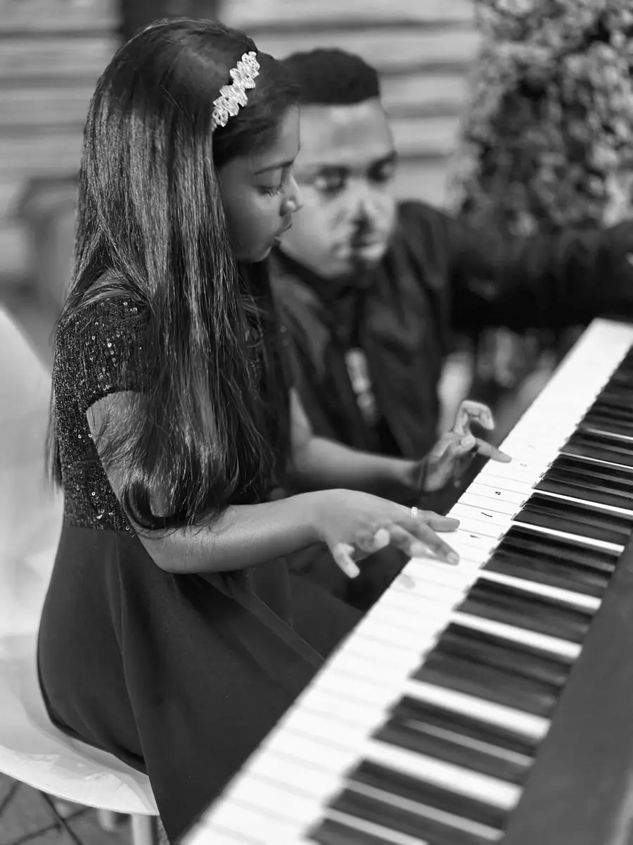A young girl playing the piano with a teacher guiding her