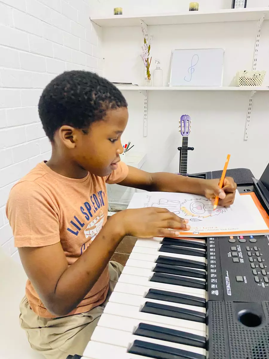 Young boy sitting at an electronic keyboard drawing in a workbook