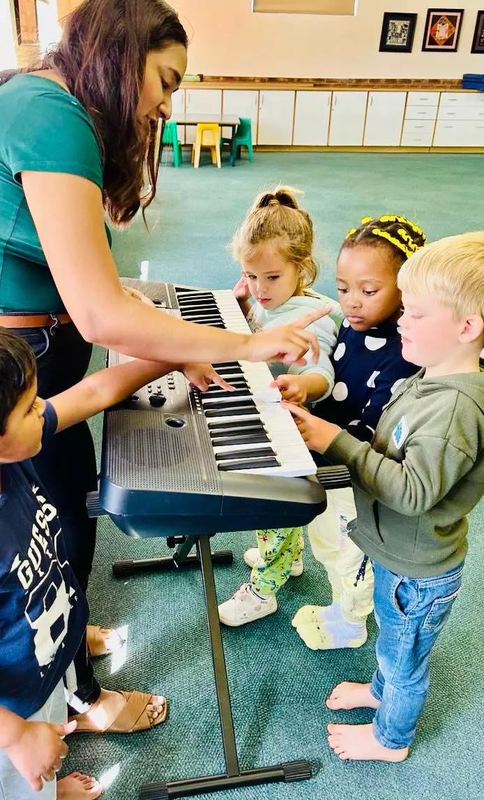 A music teacher guiding young children playing a keyboard in a classroom
