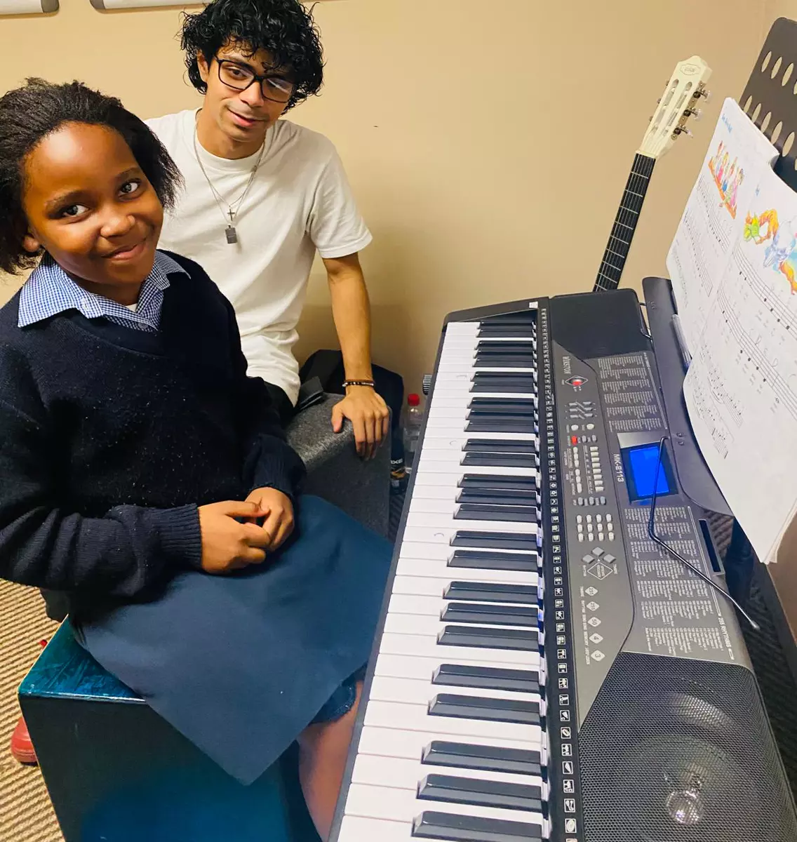 Music teacher and student sitting by an electronic keyboard