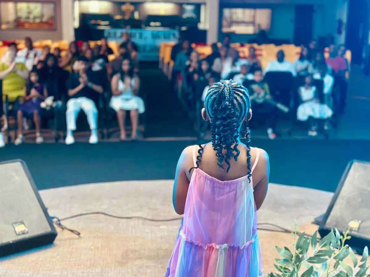 A young girl facing an audience from a stage
