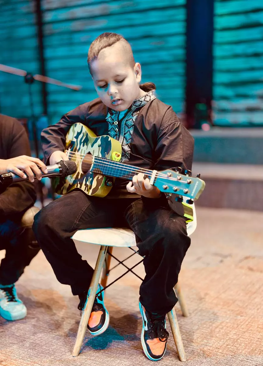 A young boy sitting on a chair and playing an acoustic guitar