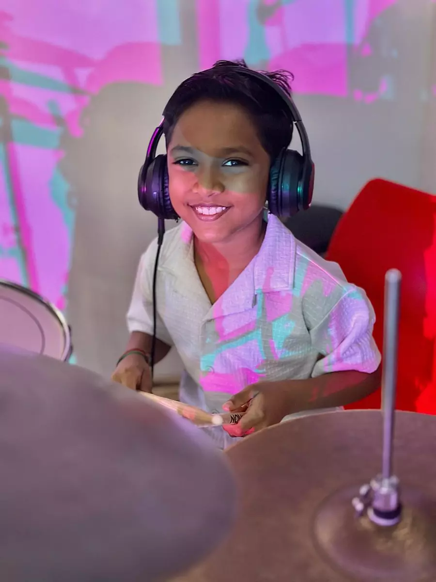 Young boy wearing headphones and smiling while playing drums