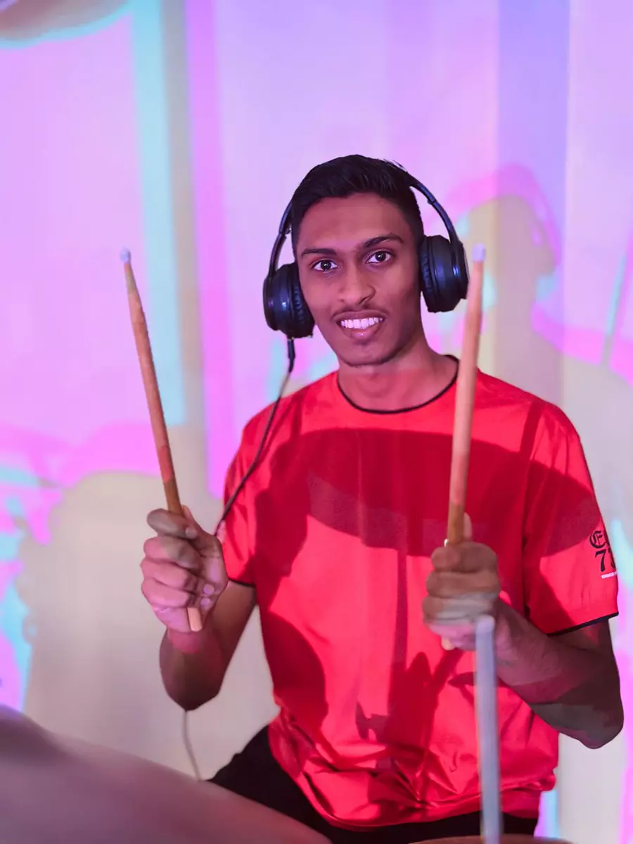 Young man wearing headphones and holding drumsticks in front of a colorful projection