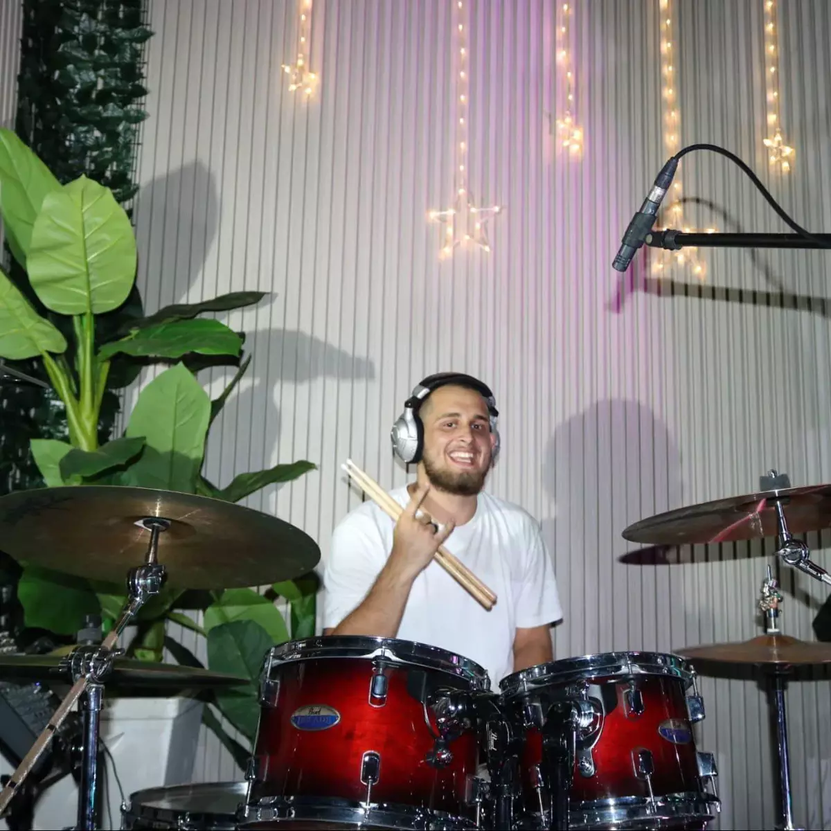 Smiling male drummer holding drum sticks behind a red drum kit